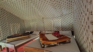 A tent-like room with patterned walls, a bed with a red blanket, and a table with folded blankets. - RIVER SIDE CAMP CHOPTA  (Pokhri)
