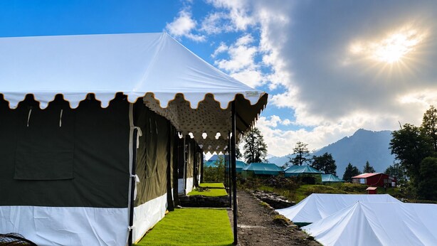 A row of tents with a clear sky and mountains in the background. - RIVER SIDE CAMP CHOPTA  (Pokhri)