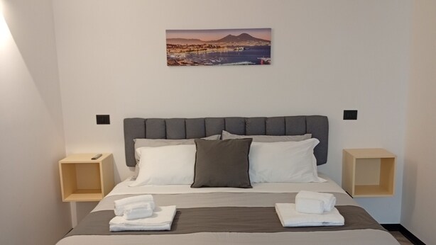 Uma cama bem arrumada com cabeceira, duas mesas de cabeceira, um quadro pendurado na parede e piso de madeira.