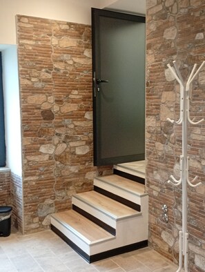 A staircase with a stone wall on one side and a coat rack on the other.