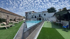 Uma piscina com espreguiçadeiras e área de bar, cercada por um edifício com parede de pedra e céu claro.