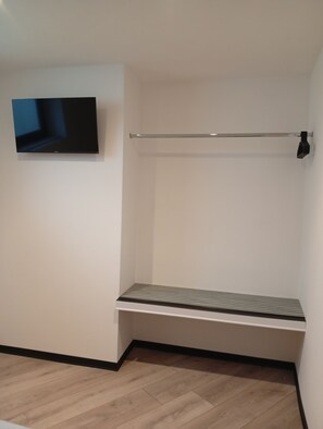 Quarto com televisão de tela plana na parede, uma barra de metal e um banco.