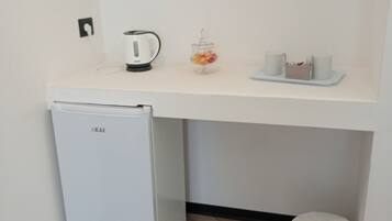 Una kitchenette compacta con un refrigerador blanco, un hervidor, un frasco pequeño de fruta y una bandeja con tazas y una cesta.
