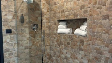 Una ducha con cerramiento de vidrio, paredes de piedra y un estante con toallas.