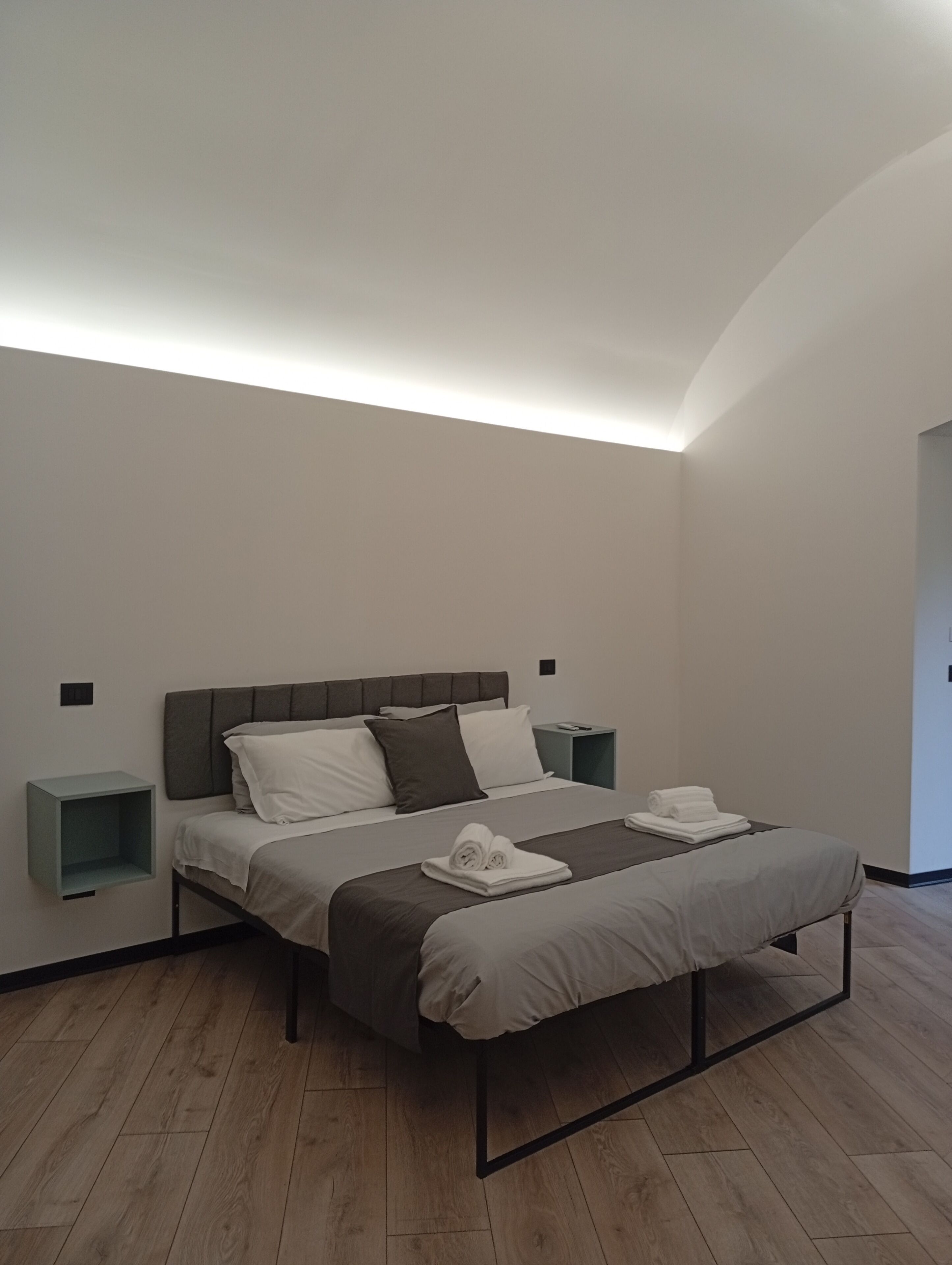 A modern bedroom with a bed, bedside tables, and a wooden floor.