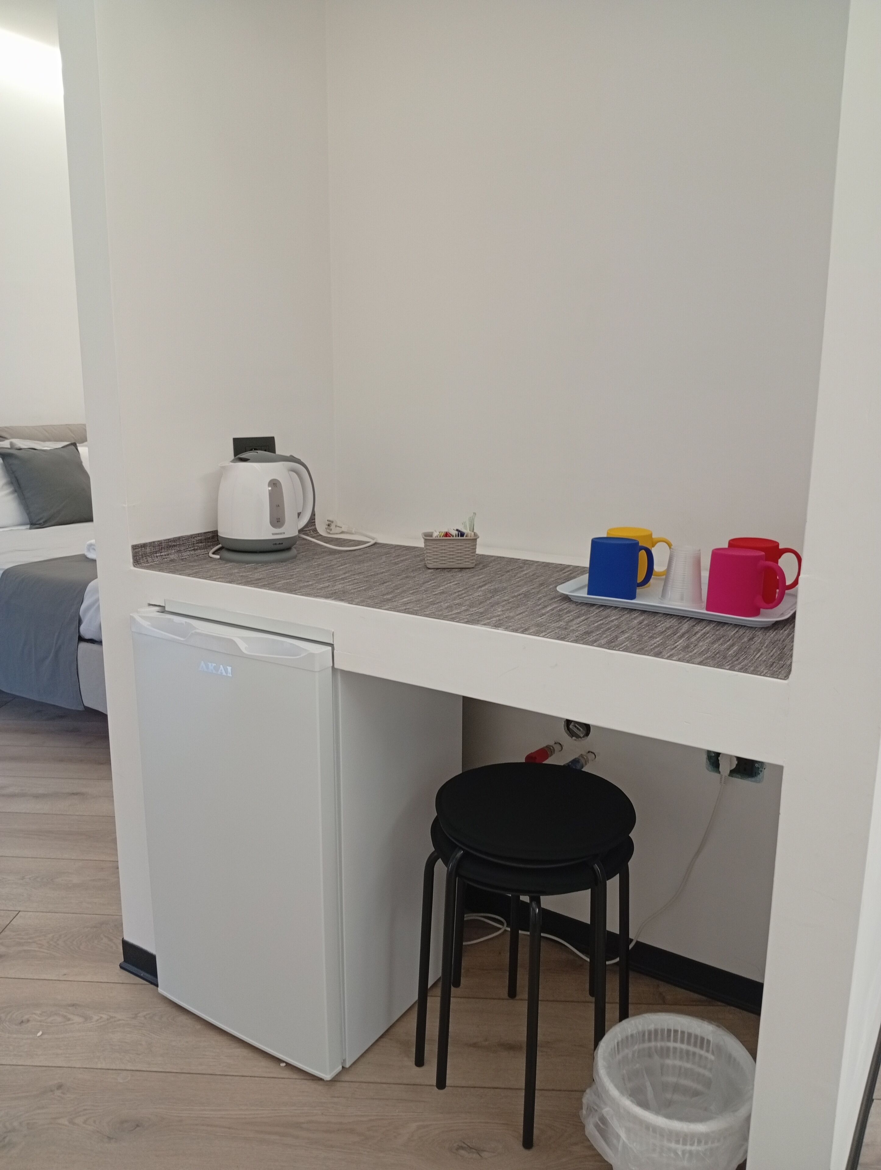 A kitchenette with a white refrigerator, a kettle, and a small stool.