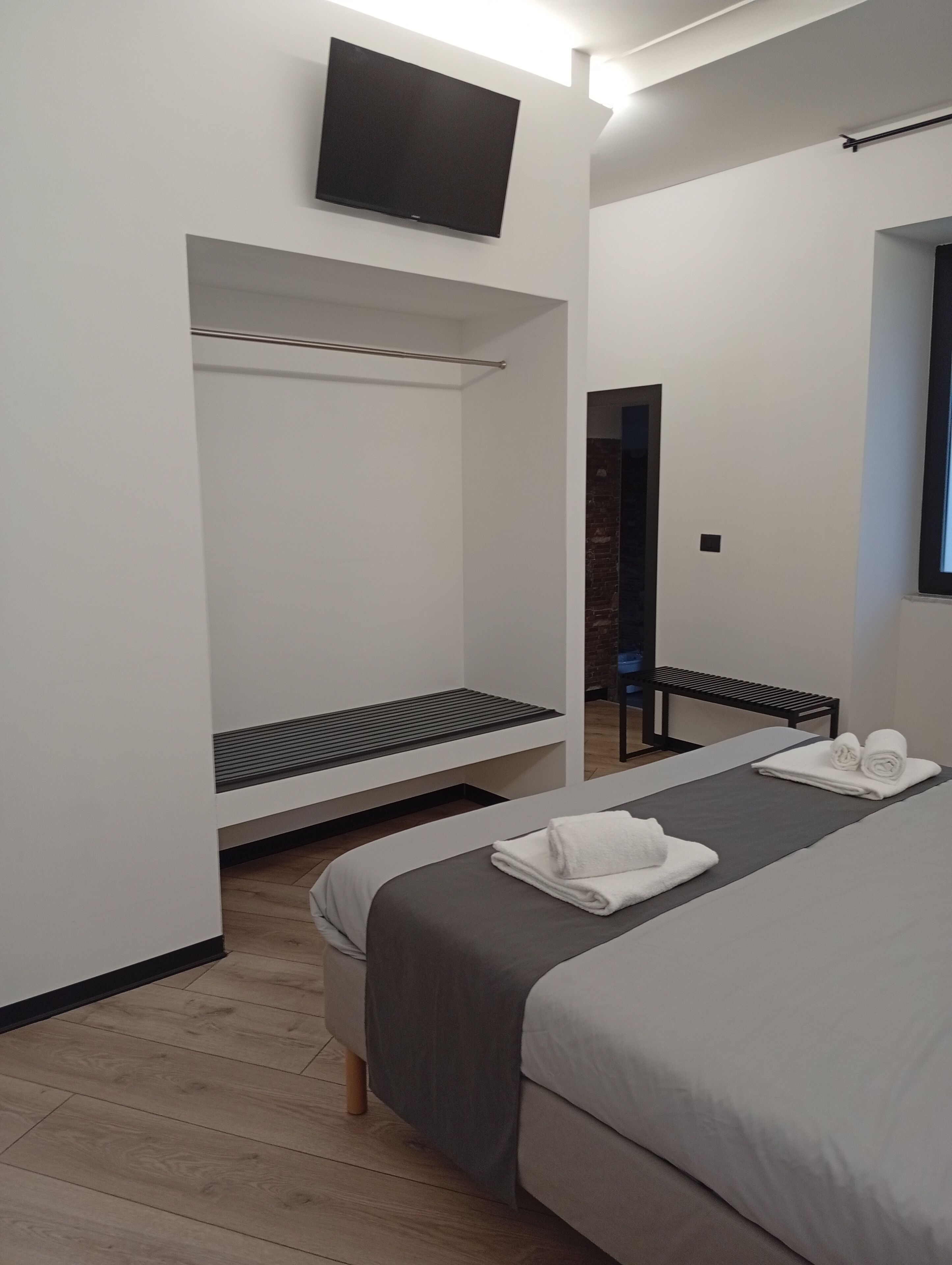 Ein modernes Hotelzimmer mit einem großen Bett, einem flachbildfernseher an der Wand, einer Sitzbank und einem Spiegel.