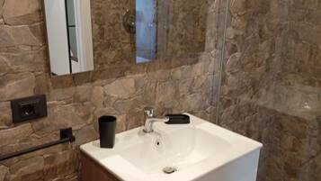 A bathroom with a stone wall, a white sink, a mirror, and a black trash bin.