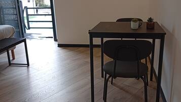 Een kamer met een houten vloer, een eettafel met twee stoelen, een kleine potplant en een aan de muur hangend schilderij.