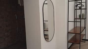 Een kamer met een houten vloer, een witte muur, een spiegel met een zwarte lijst en een metalen schapenkast met een plant.