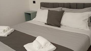 Una cama doble con cabecera gris, ropa de cama blanca y gris, y dos toallas enrolladas sobre la cama.