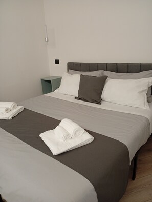 A double bed with a grey headboard, white and grey bedding, and two rolled towels on the bed. - Borgo Double V (Napoli)