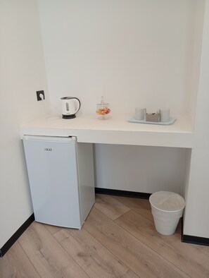A compact kitchenette with a small refrigerator, a kettle, a glass jar of candies, and a tray with cups and a basket. - Borgo Double V (Napoli)