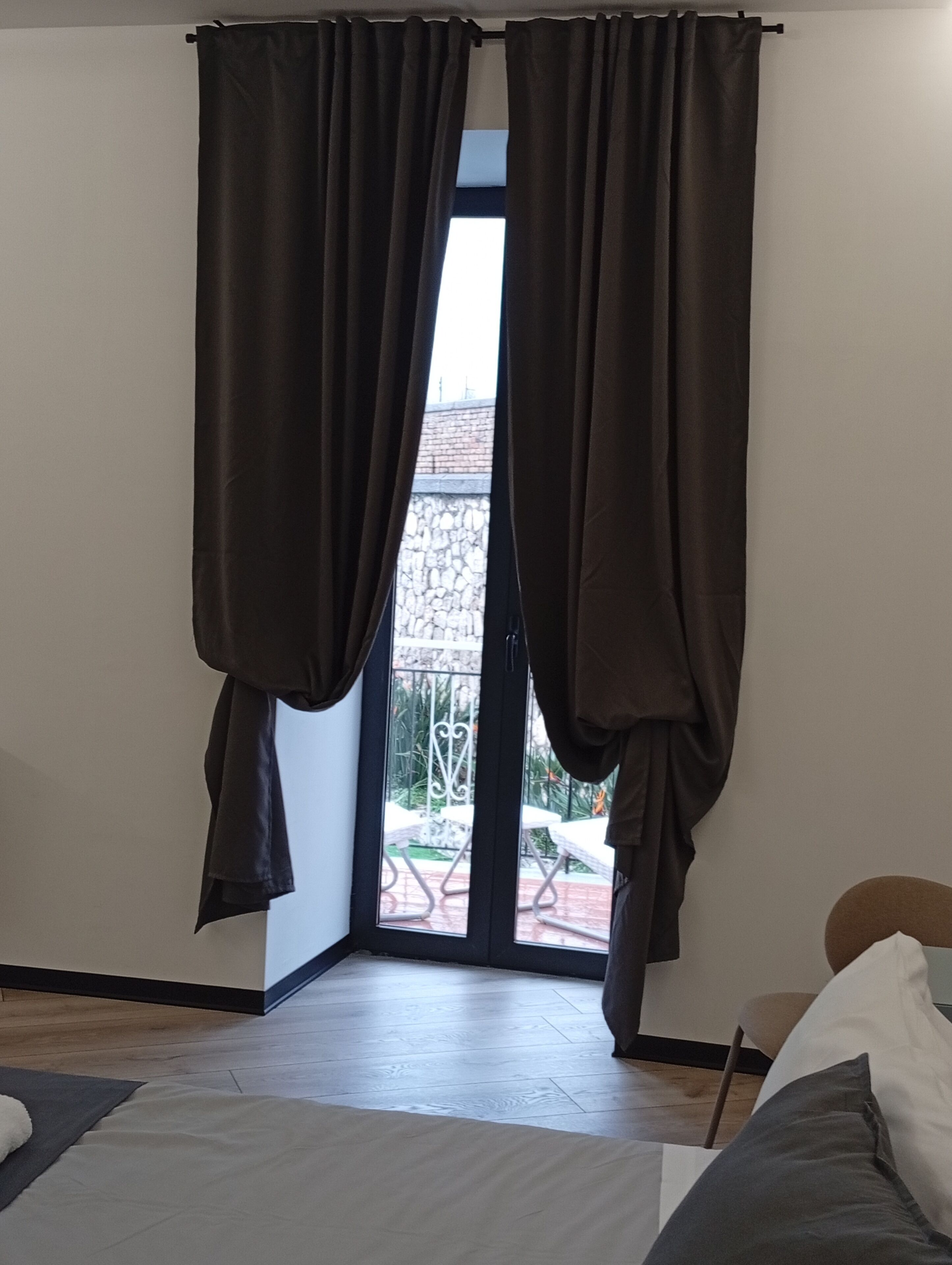 Una stanza con una grande finestra, un pavimento in legno e un letto con copriletto bianco.
