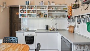 A compact kitchen with white cabinets, a built-in oven, a dishwasher, and a dining area with a wooden table and chairs. - Relax na Šumavě by Interhome (Kasperske Hory)