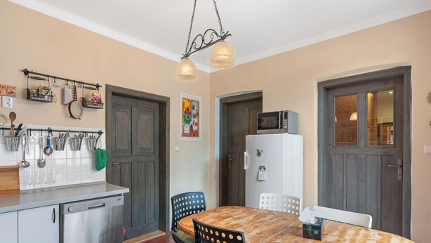 A compact kitchen with a wooden dining table, chairs, a refrigerator, and a microwave. - Relax na Šumavě by Interhome (Kasperske Hory)