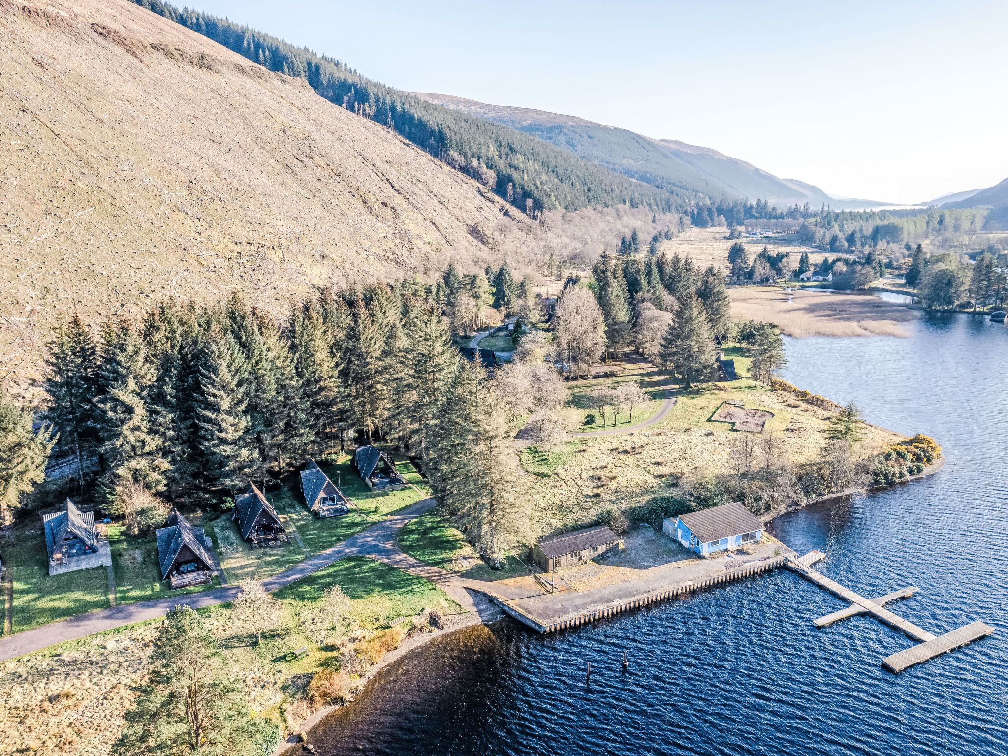 Una propiedad junto al lago con cabañas, un muelle y una ladera boscosa.