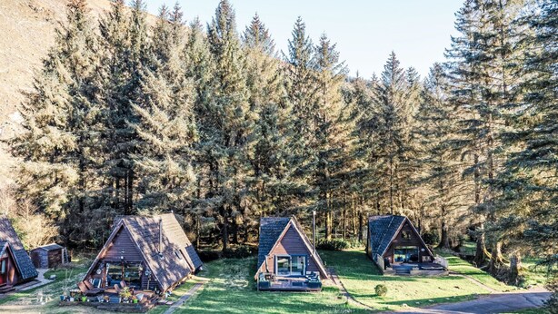 A row of small, triangular-roofed cabins surrounded by dense forest. - Pine Needle Lodge by Interhome (Invergarry)