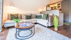 A modern living room with a sectional sofa, a coffee table, and a kitchen area in the background. - Pine Needle Lodge by Interhome (Invergarry)