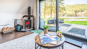 A room with a fireplace, a Monopoly board game, and a view of a forested area. - Pine Needle Lodge by Interhome (Invergarry)