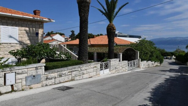 A residential street with stone walls, a paved road, and a clear view of the sea in the background. - One Bedroom Apartment with Terrace & Garden View (Supetar)