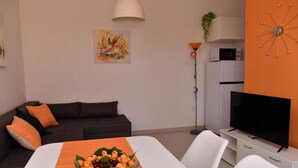 A modern living room with a dark sofa, a white TV stand, and a dining table with a fruit bowl. - One Bedroom Apartment with Terrace & Garden View (Supetar)