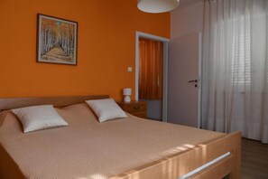 A bedroom with a large bed, a nightstand, a painting on the wall, and a door with curtains.