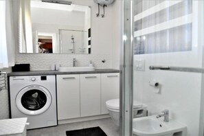 A modern bathroom with a washing machine, toilet, sink, and a glass shower enclosure.