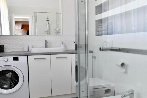 Een moderne badkamer met een douchecabine van glas, een ingebouwde wasmachine en een witte wastafel.