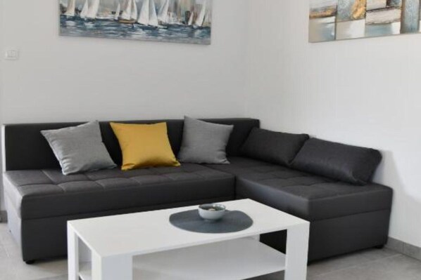 A modern living room with a dark grey sectional sofa, a white coffee table, and artwork on the walls.