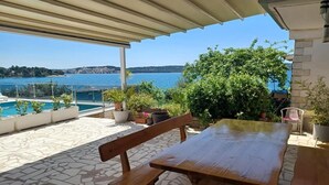An outdoor patio with a wooden table and bench, potted plants, and a view of a lake and distant hills. - Two-bedroom Apartment With Sea View (A1) (Trogir)