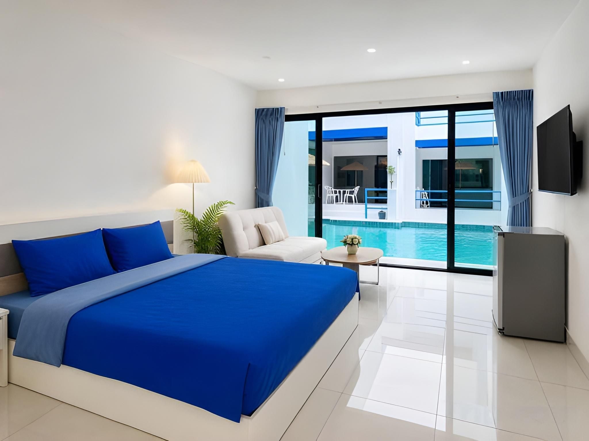 A hotel room with a large bed, a seating area, a small table, a TV, and a view of a swimming pool.
