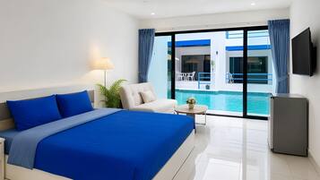 A hotel room with a large bed, a seating area, a small table, a TV, and a view of a swimming pool.
