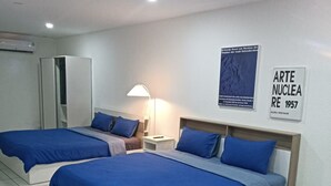 Quarto de hotel com duas camas, uma mesa de madeira e um vaso de planta.