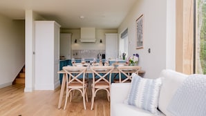 Una cucina moderna con mobili bianchi, un'area pranzo con sedie in legno e un divano bianco con cuscini decorati.