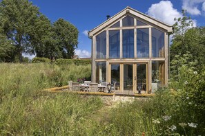 Une structure en bois dotĂ©e dâun toit en verre, avec un espace patio et du mobilier dâextĂ©rieur.