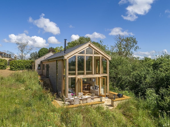 Una casa de madera con un porche de cristal, un patio con muebles de exterior y una chimenea.