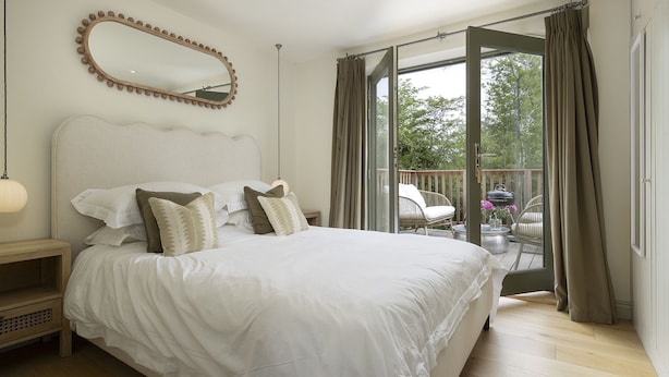 Une chambre avec un grand lit, un miroir et un balcon aménagé avec du mobilier d’extérieur.
