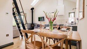 Un coin repas avec une table en bois dressée pour quatre personnes, un vase rempli de fleurs et un escalier menant à l’étage supérieur.