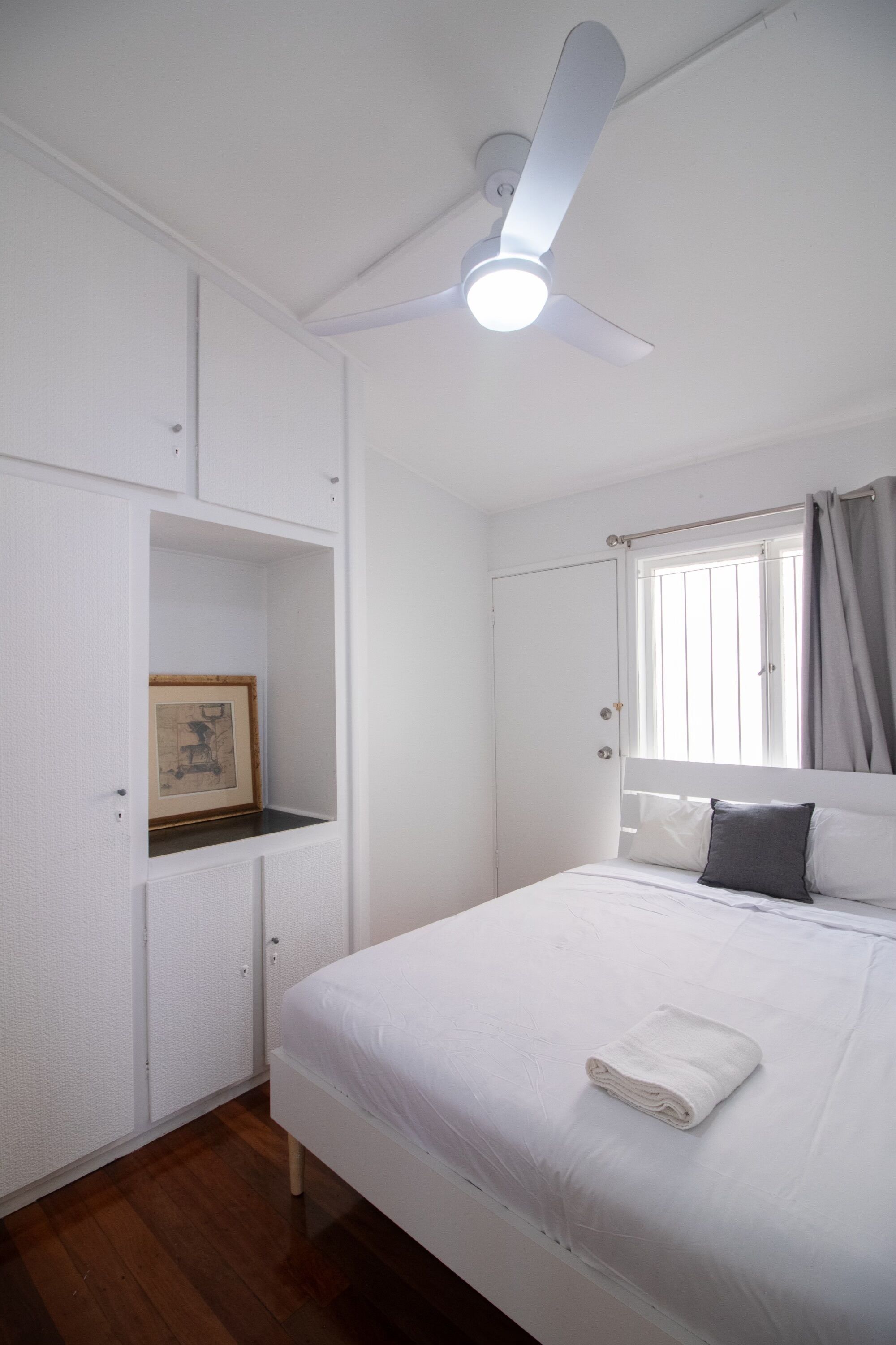 A bedroom with a bed, a ceiling fan, a window with curtains, and a wardrobe.