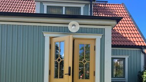 Een herenhuis met twee verdiepingen, voorzien van een rood pannendak, een gele voordeur met ruitpanelen en een klein portaal met treden.