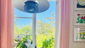 Een ronde houten tafel met stoelen, een hanglamp en potplanten op een vensterbank.