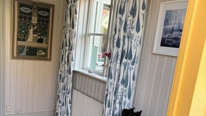 Een kamer met houten vloer, een witte radiator, een raam met behang gordijnen, een plank met schoenen en een lijst met een foto aan de muur.