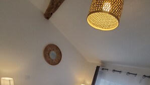 A bedroom with a large bed, two bedside tables with lamps, a ceiling light fixture, a window with curtains, and a wall-mounted mirror.