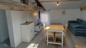 A spacious room with a wooden ceiling, a skylight, a dining table with chairs, a sofa, and a small cabinet.