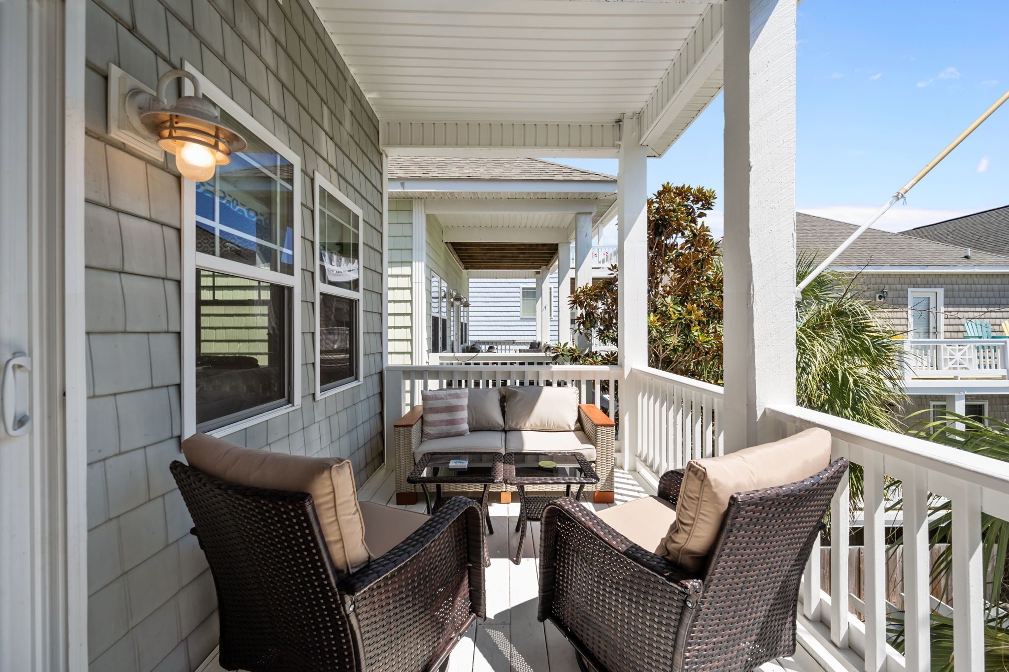 A covered porch with wicker furniture and a table, overlooking a residential area.