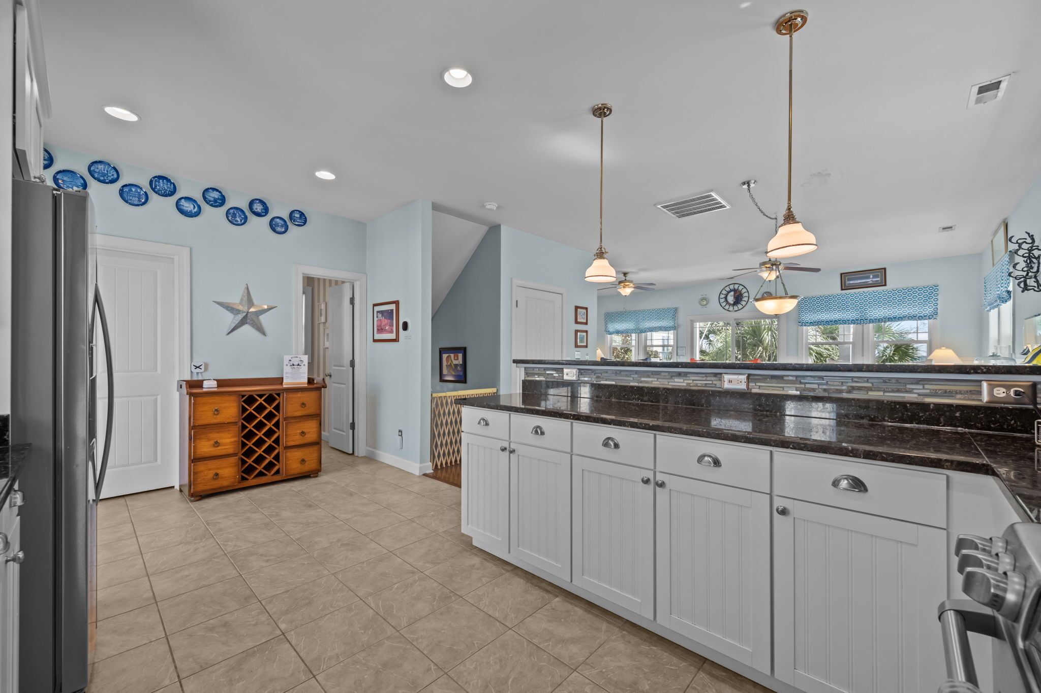 A kitchen with white cabinets, a black countertop, and a wooden chest of drawers. There are blue decorative plates on the wall and a star decoration.