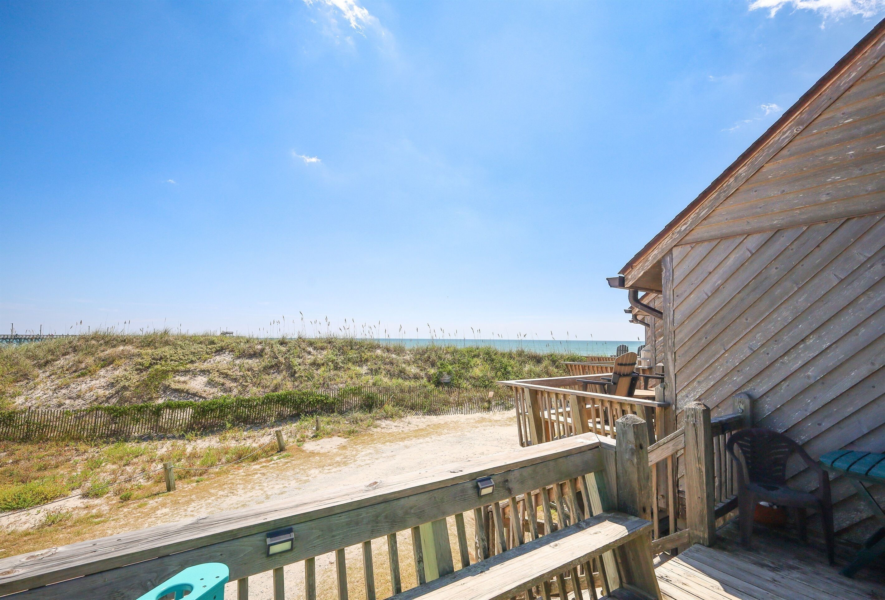 A wooden deck with outdoor furniture overlooking a beach with dunes and the ocean.