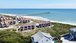 Un quartier résidentiel en bord de mer, avec des maisons donnant sur la plage, une jetée qui s’avance dans la mer et une piscine.