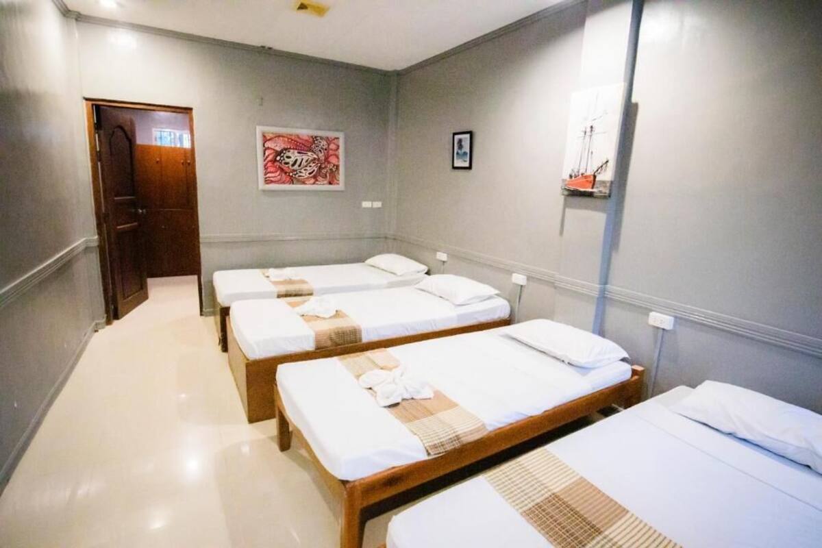 Une chambre d’hôtel avec trois lits simples, une porte, un mur orné d’un tableau et une petite étagère sur laquelle est posé un objet décoratif.